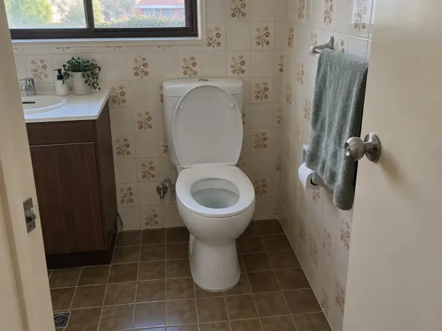 Clean white toilet in a tiled bathroom with vanity, towel rail and window in Wolli Creek
