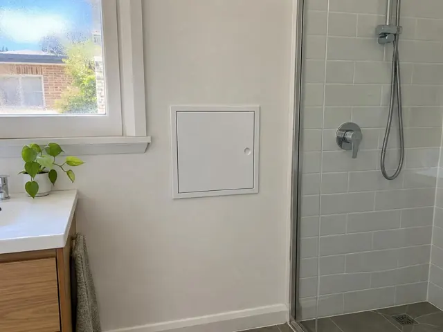 Bathroom wall with small access panel beside a tiled shower in Kogarah