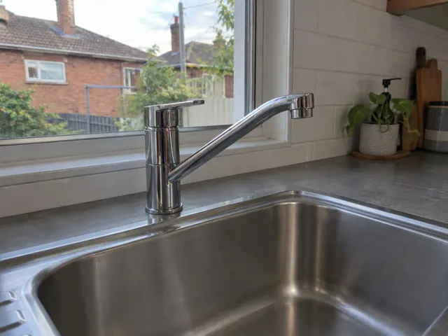 Chrome kitchen mixer tap above a stainless sink with tiled splashback and window in Tempe